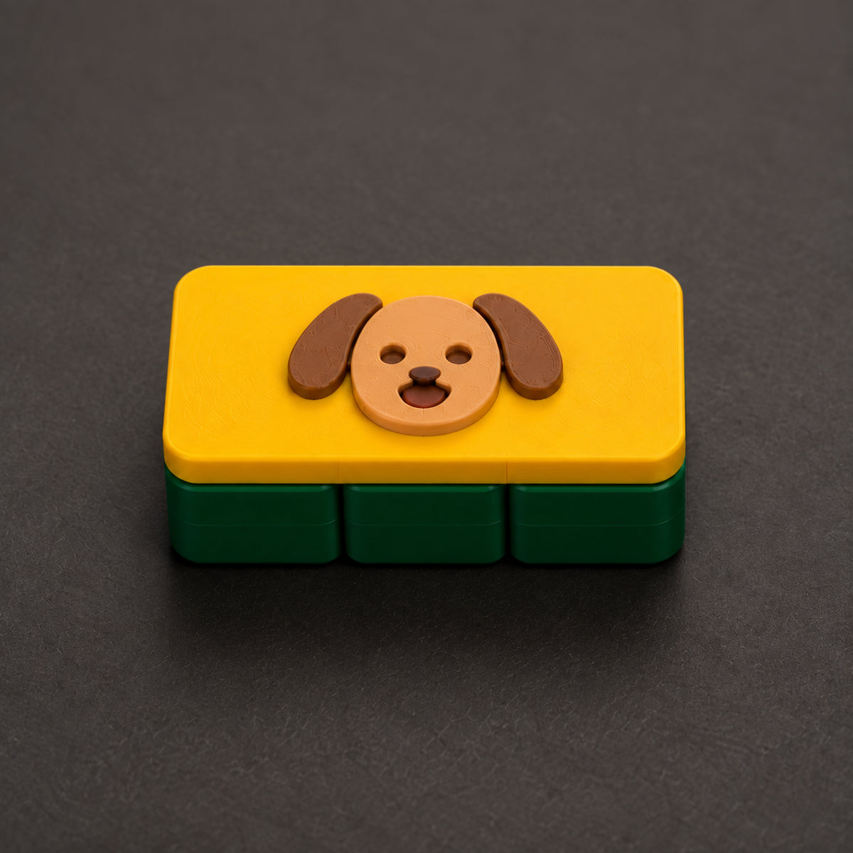 Tan puppy on a yellow cap and dark green three-square base — one large clicker. Generated design concept, not a printed sample.