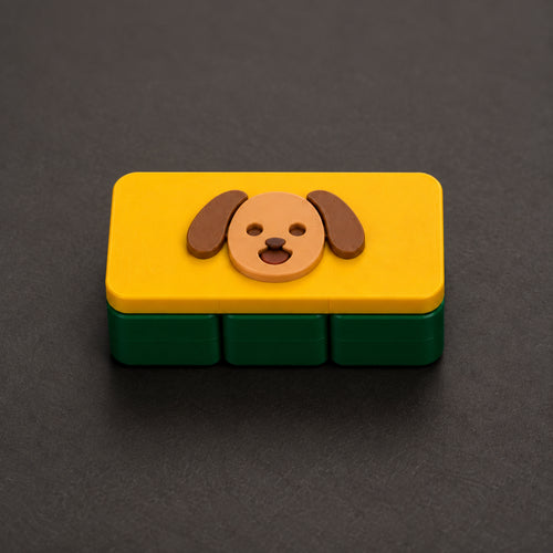 Tan puppy on a yellow cap and dark green three-square base — one large clicker. Generated design concept, not a printed sample.